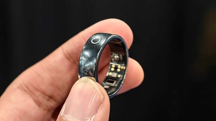 A sleek circular smart ring worn on an index finger with green optical sensor light reflecting