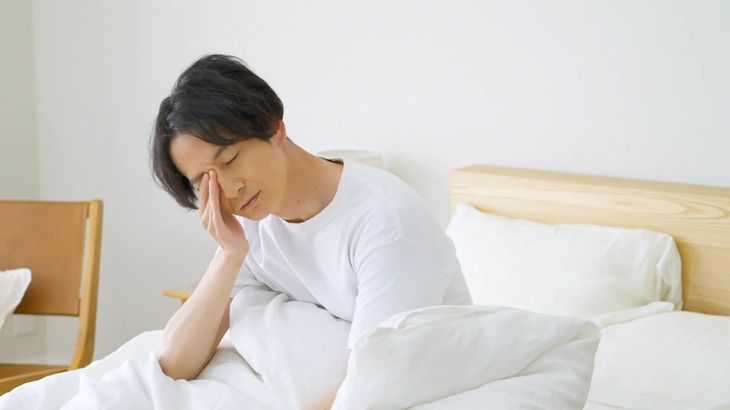Tired woman rubbing her eyes while sitting in bed in the morning